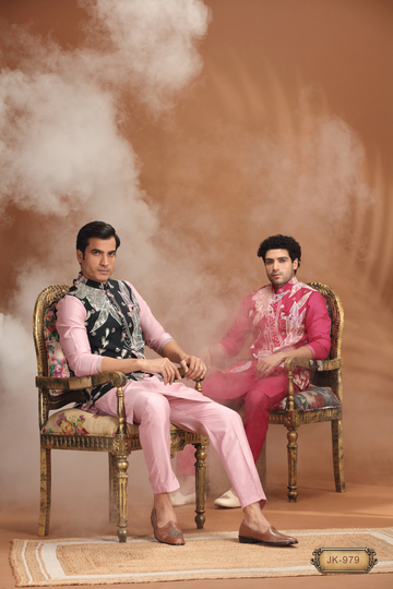 Two men in embroidered pink and red traditional South Asian sherwanis, seated on antique floral chairs with smoke effect.